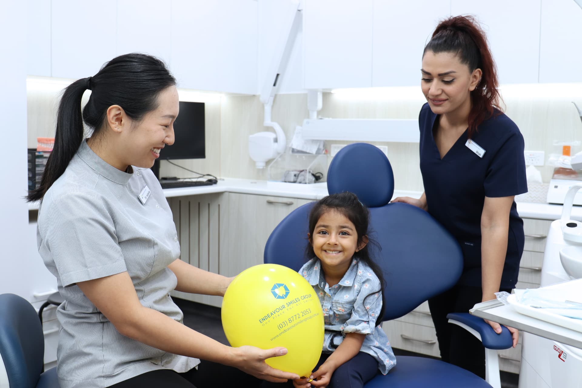 Dentist and dental assistant with a smiling young patient holding an Endeavour Smiles Group balloon